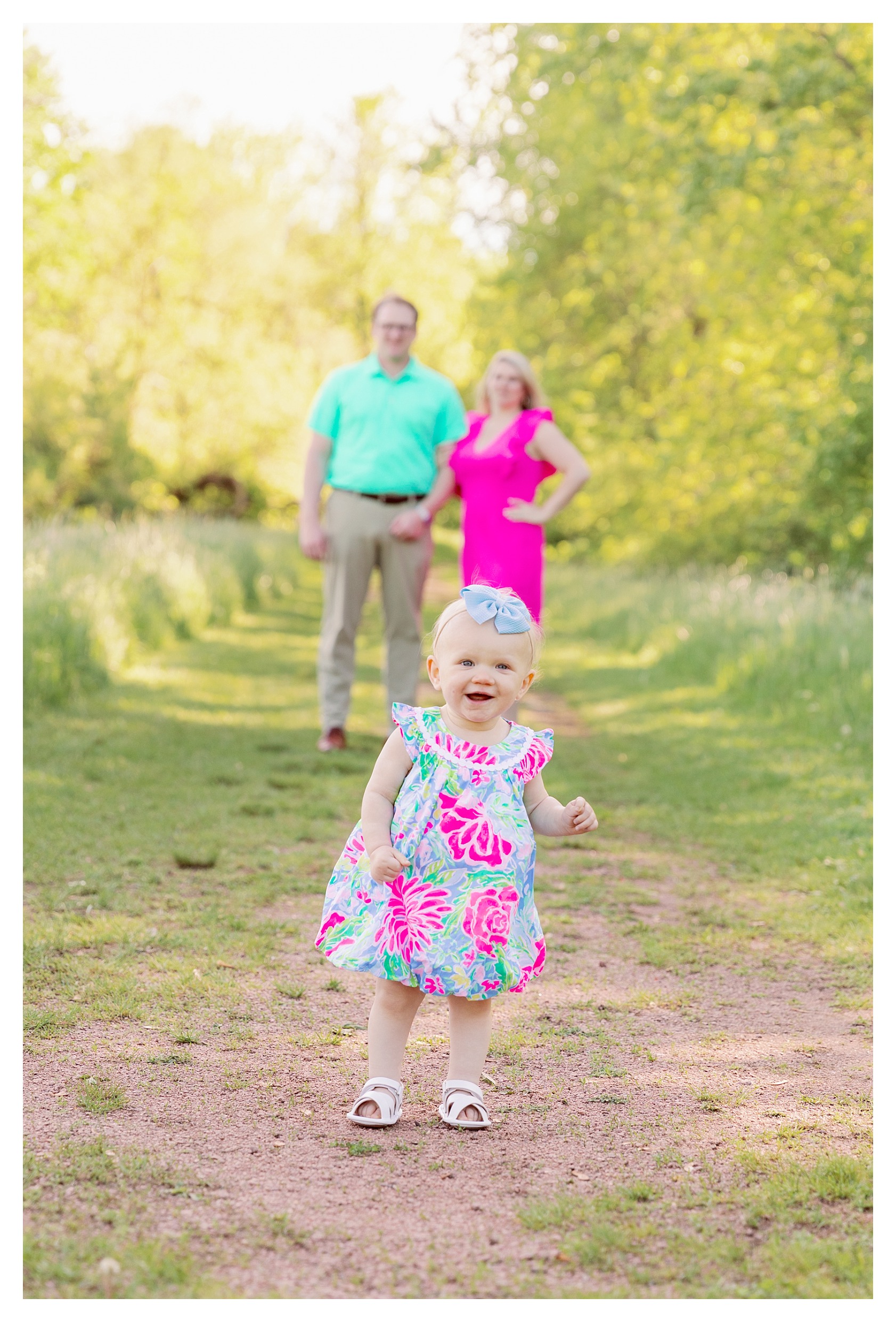 One year old little girl smiles while mom and dad are in background